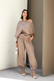 Woman wearing a beige off-shoulder top and wide-leg pants against a neutral wall.
